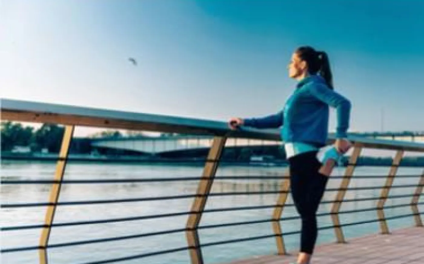 A woman stretches on a wooden dock beside calm water, enjoying the serene outdoor environment.