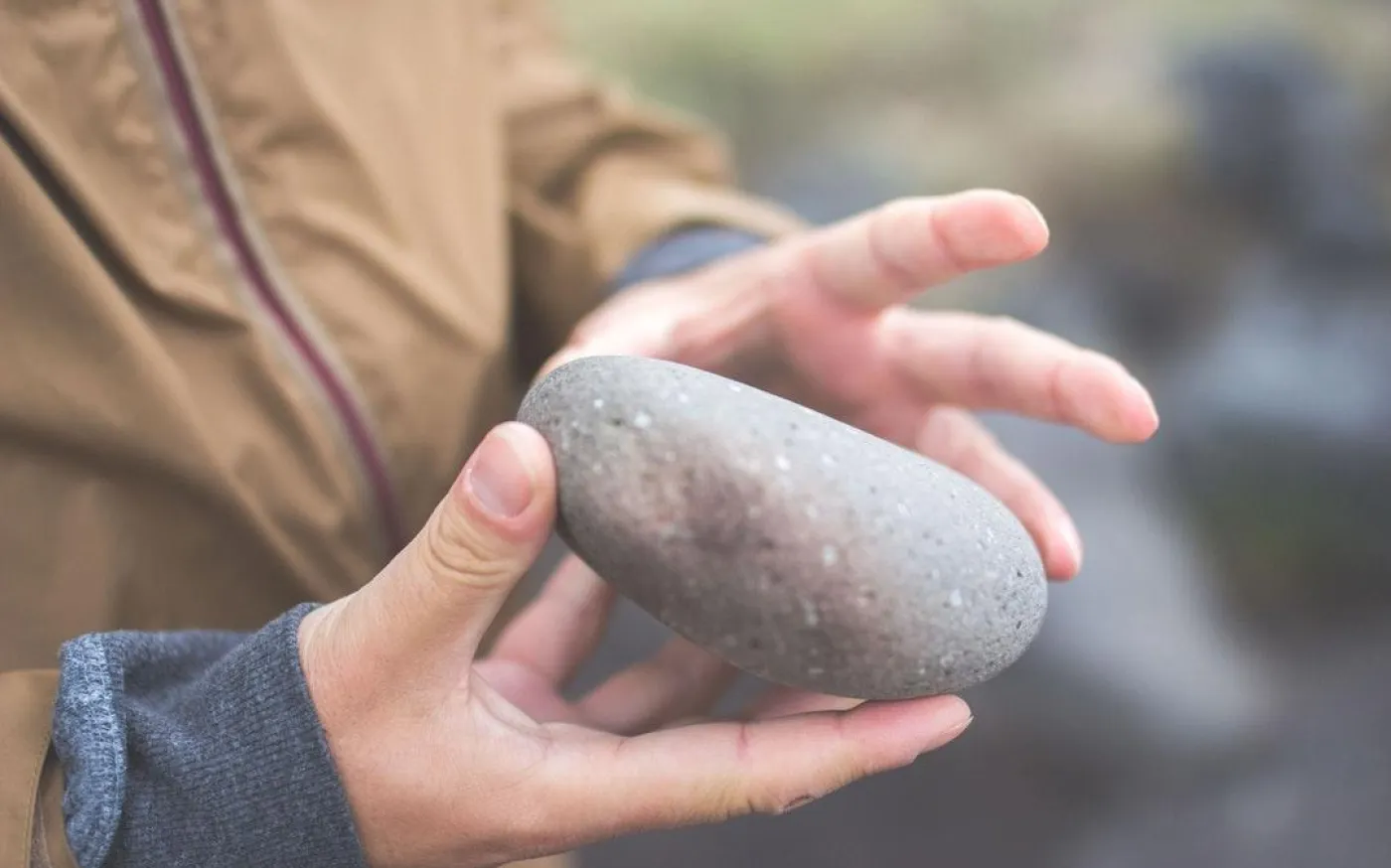 A person gently cradles a smooth stone in their hands, showcasing its natural texture and shape.