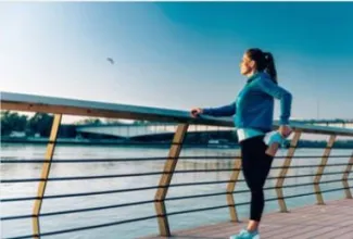 A woman stretches on a wooden dock beside calm water, enjoying the serene outdoor environment.