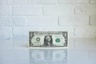 A one dollar bill placed on a table in front of a textured white brick wall.