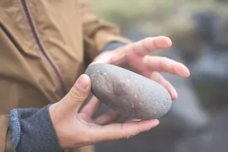 A person gently cradles a smooth stone in their hands, showcasing its natural texture and shape.