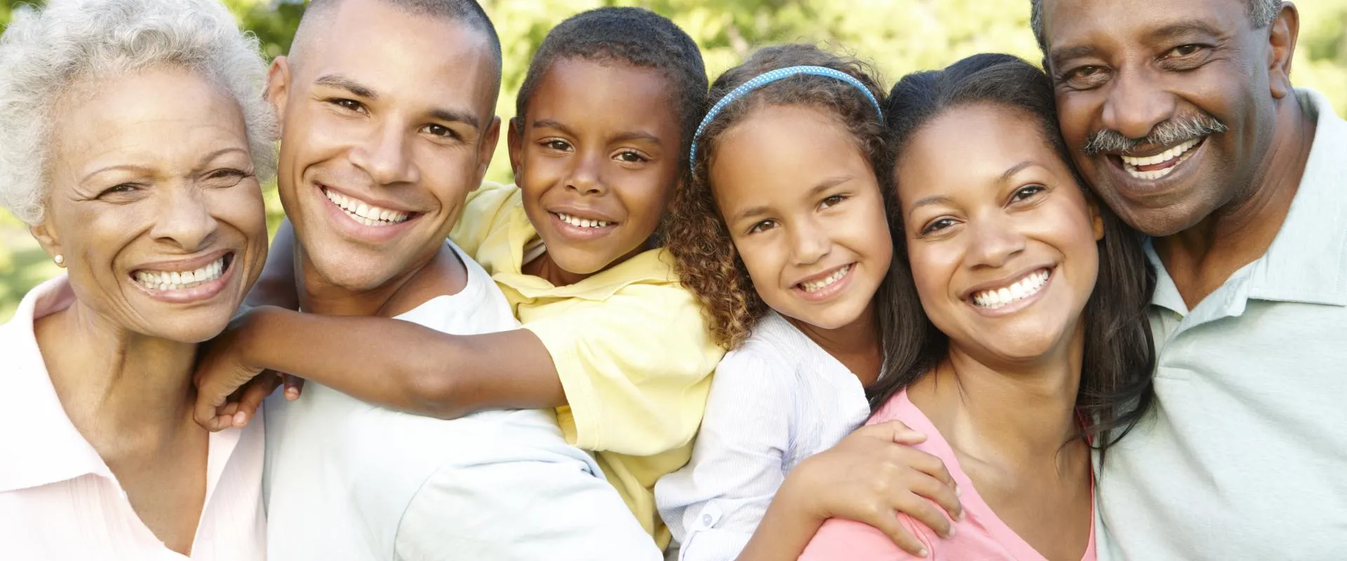 A family of four, including two adults and two children, smiling together outdoors.