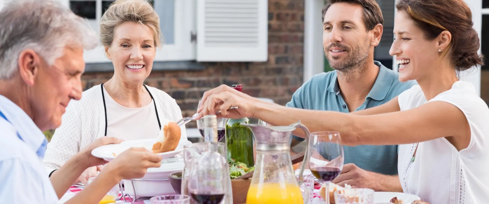  diverse group of people enjoying a meal together at a table filled with various dishes and drinks.