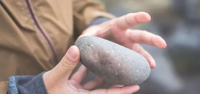 A person gently cradles a smooth stone in their hands, showcasing its natural texture and shape.